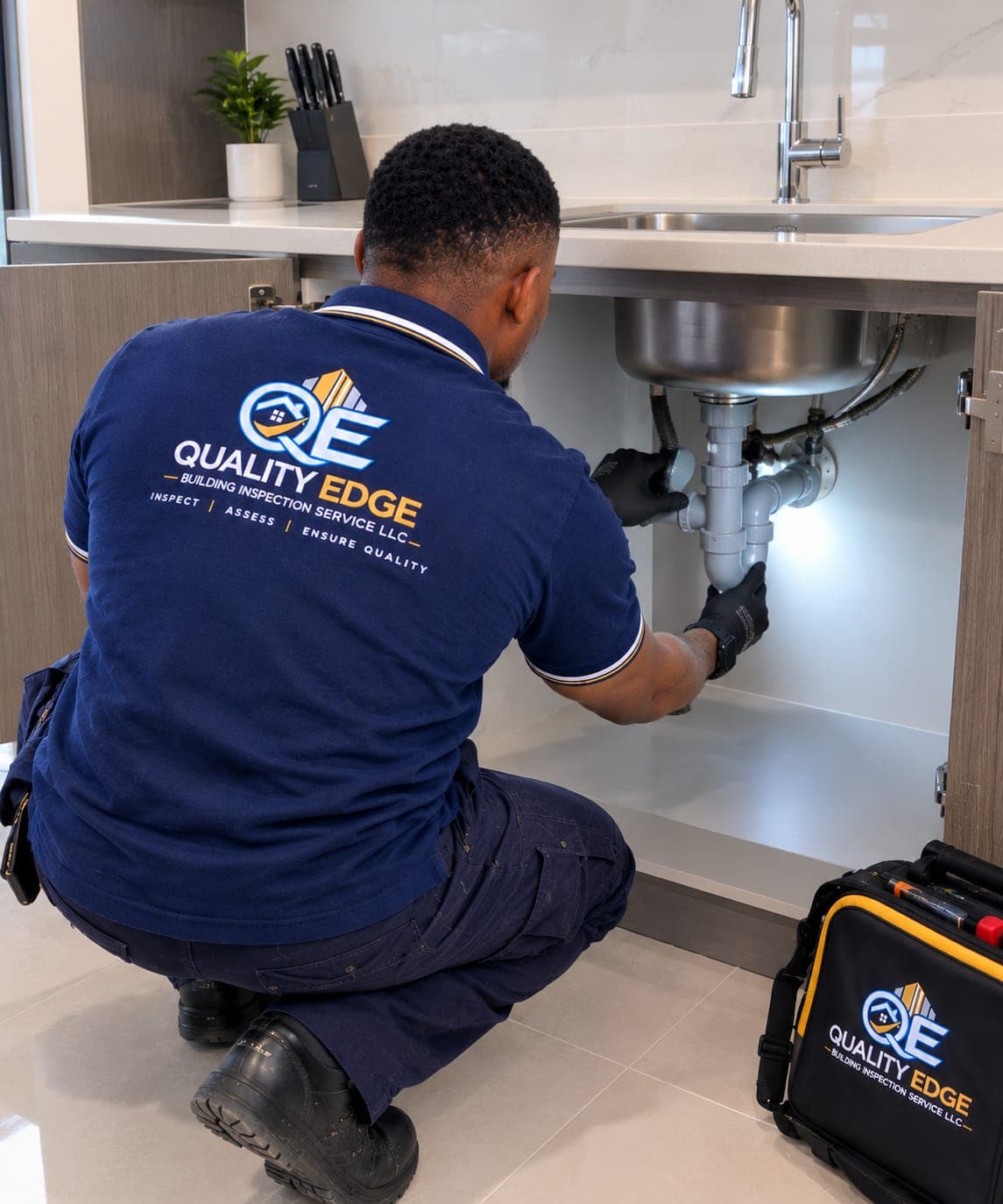 An inspector examining pipework beneath a kitchen sink.